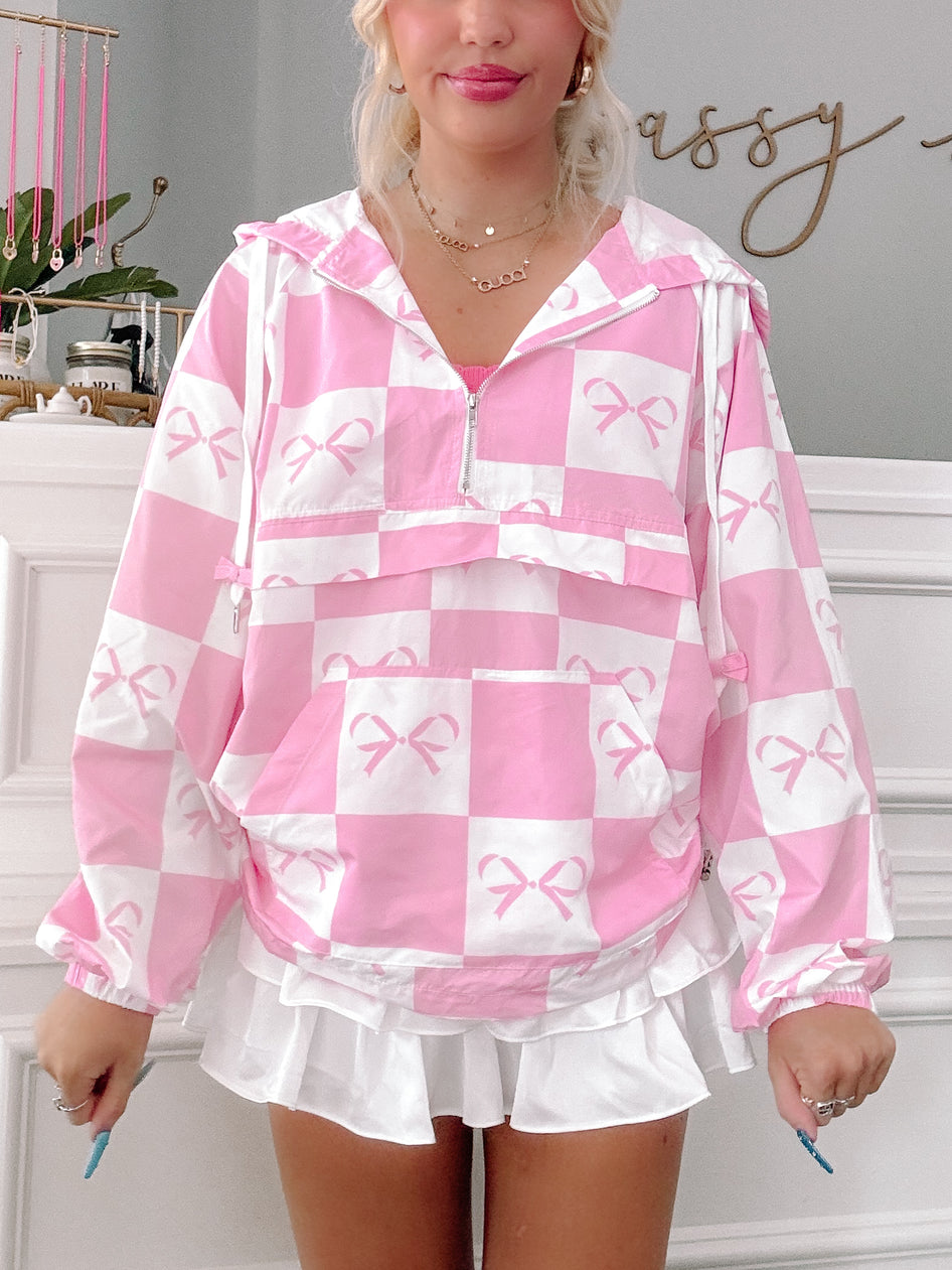 Pink checkered windbreaker with bow print, shown on model.
