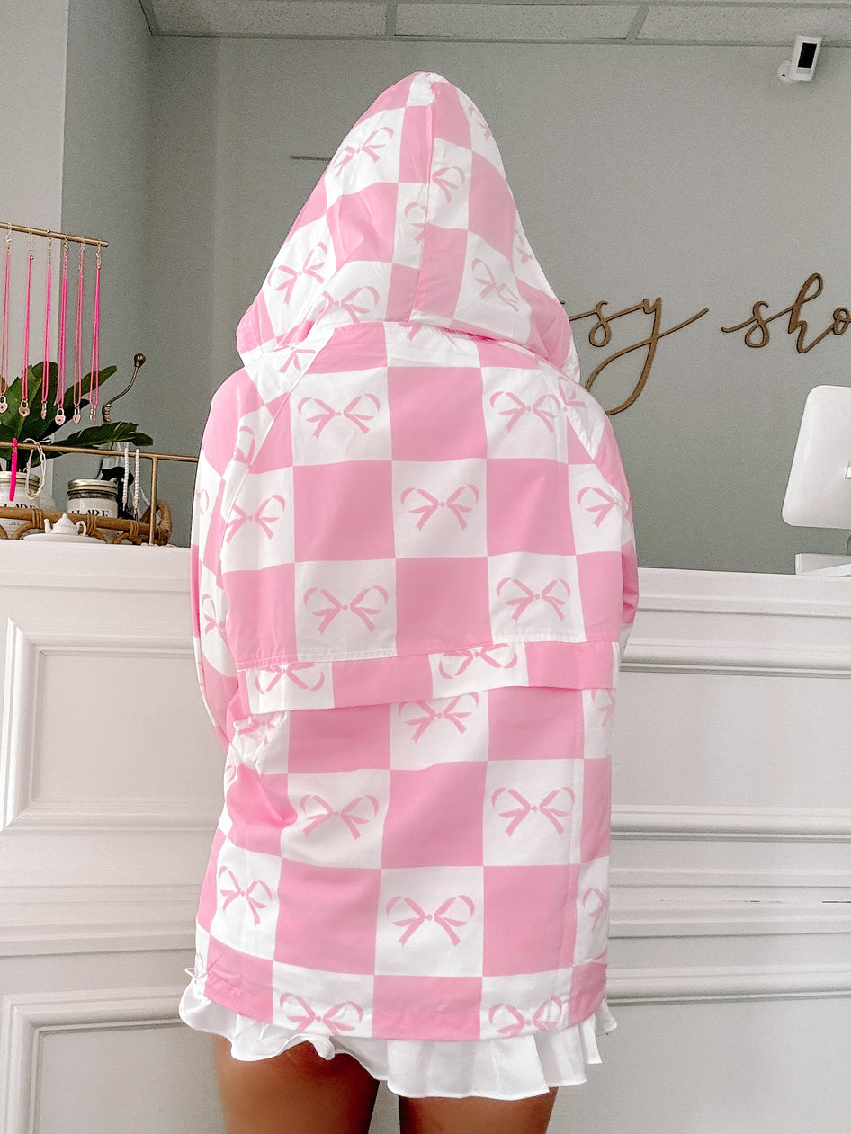 Pink checkered windbreaker with bow print, hooded, shown from the back in a shop.
