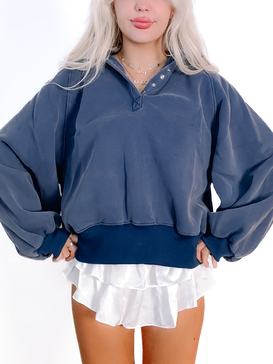 Navy blue pullover sweatshirt with balloon sleeves and a banded hem, styled with a white ruffled skirt.