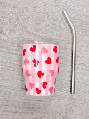 Pink tumbler with red hearts and gingham pattern, includes metal straw.
