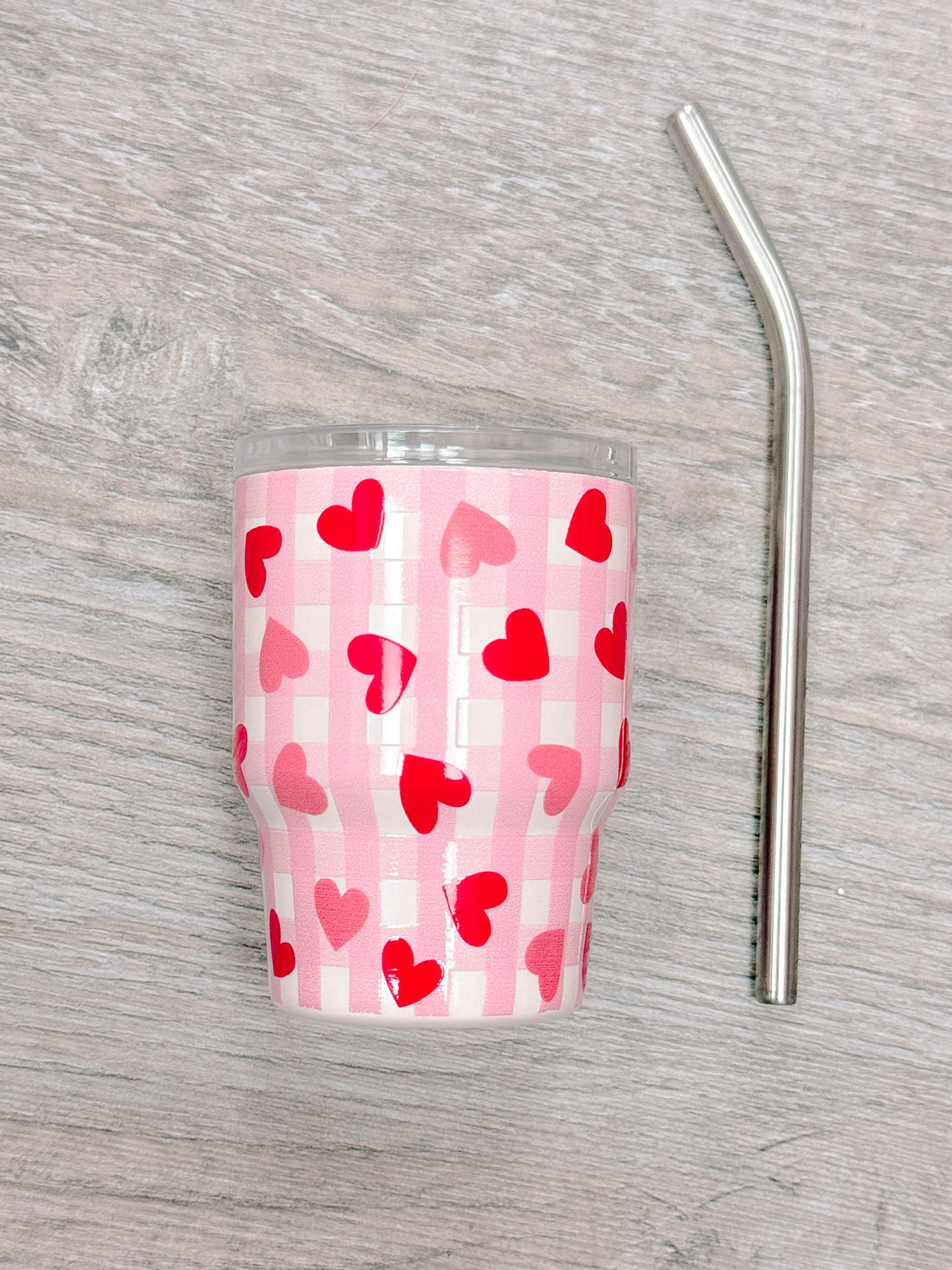 Pink tumbler with red hearts and gingham pattern, includes metal straw.
