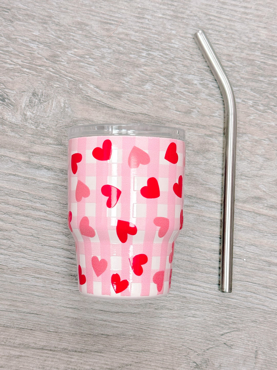 Pink tumbler with red hearts and gingham pattern, includes metal straw.
