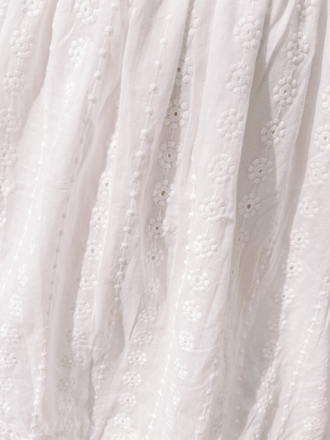 White eyelet dress fabric detail; delicate floral embroidery.
