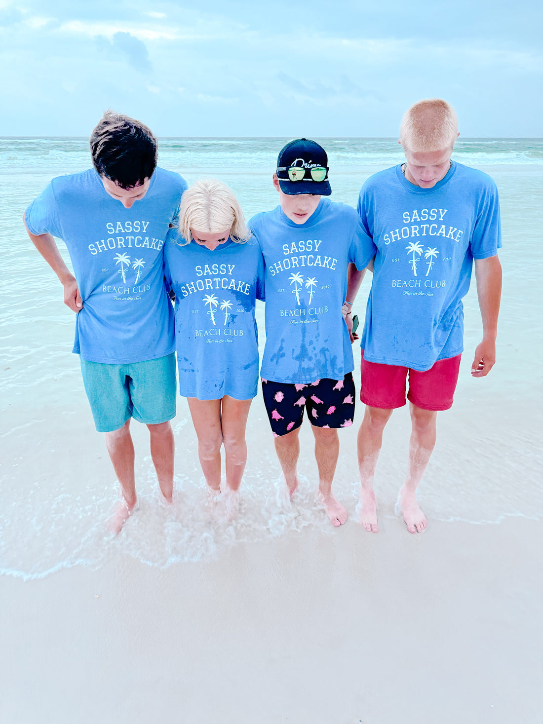 Group wearing matching light blue beach shirts at the ocean's edge.
