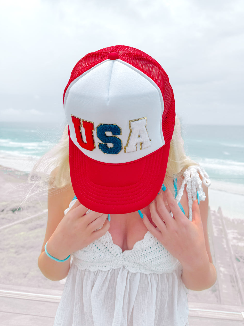 Red, white, and blue "USA" trucker hat worn at the beach.
