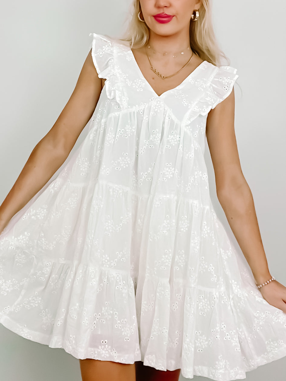 White eyelet mini dress with tiered ruffle details and sleeveless V-neck.

