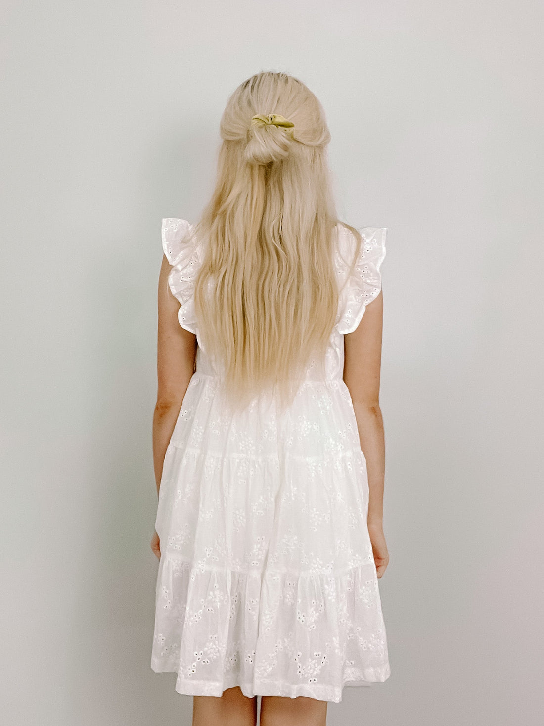White eyelet dress, tiered skirt, rear view against a light background.
