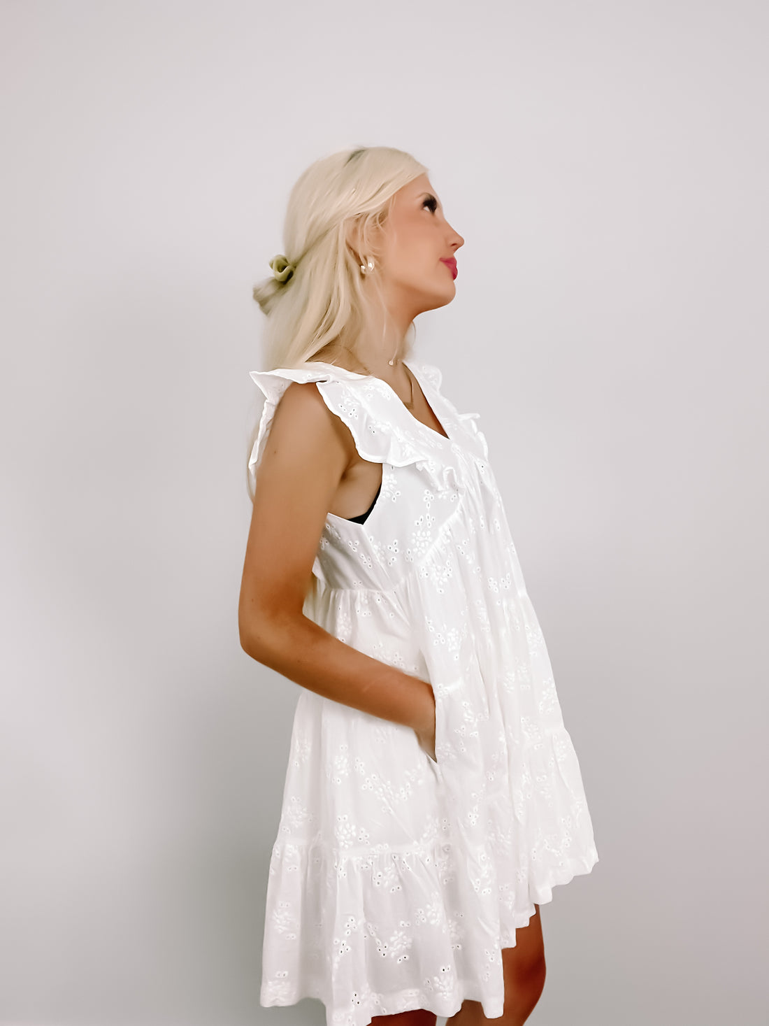 White eyelet mini dress with ruffled details, shown on a model against a neutral backdrop.
