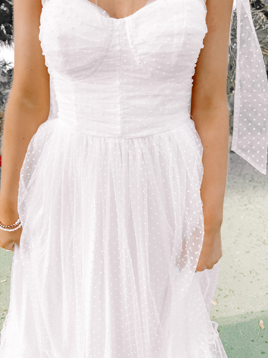 White eyelet midi dress with delicate shoulder straps, shown outdoors.
