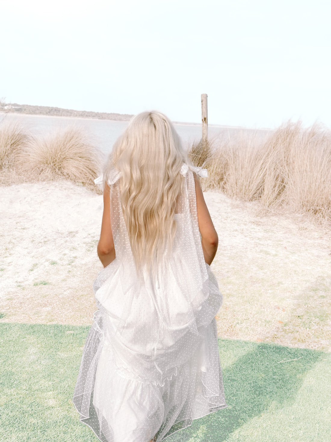 White eyelet mini dress with sheer overlay, worn outdoors near water.
