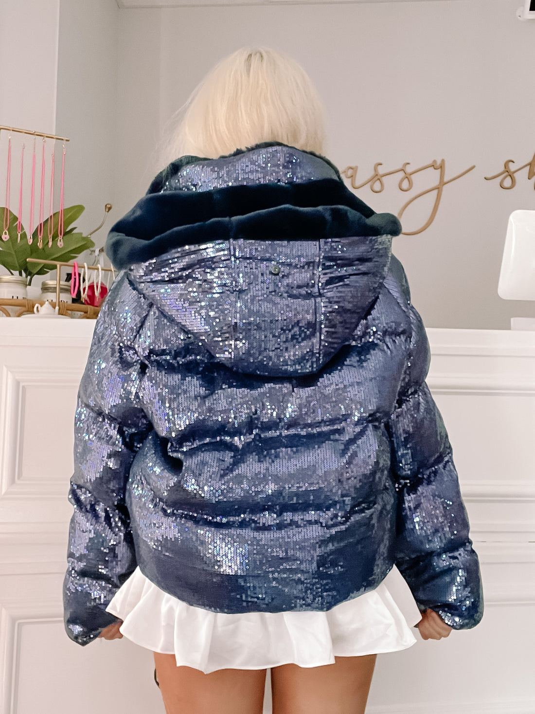 Sequin puffer jacket with a faux fur-lined hood, shown from the back in a shop setting.
