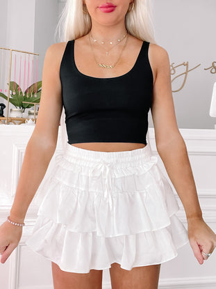 Model wearing a black tank top and white tiered ruffle skirt.
