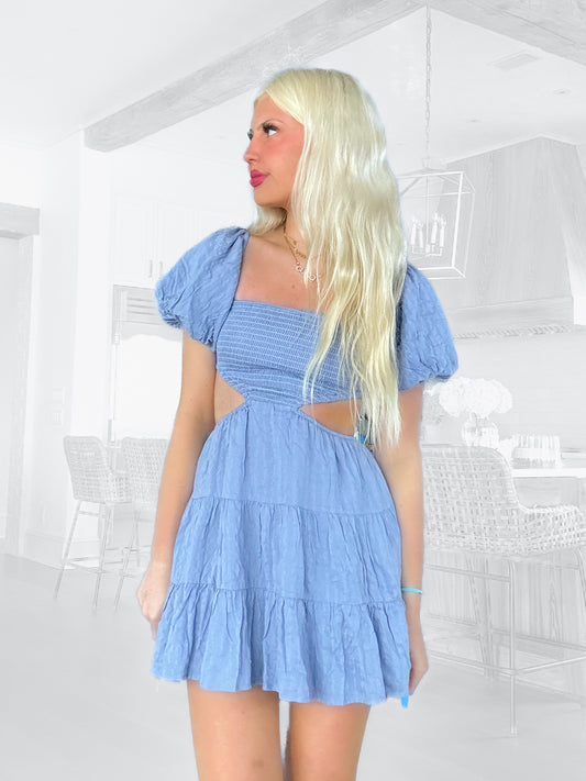 Cutout mini dress in slate blue, tiered ruffle skirt, puff sleeves, shown in a modern kitchen setting.