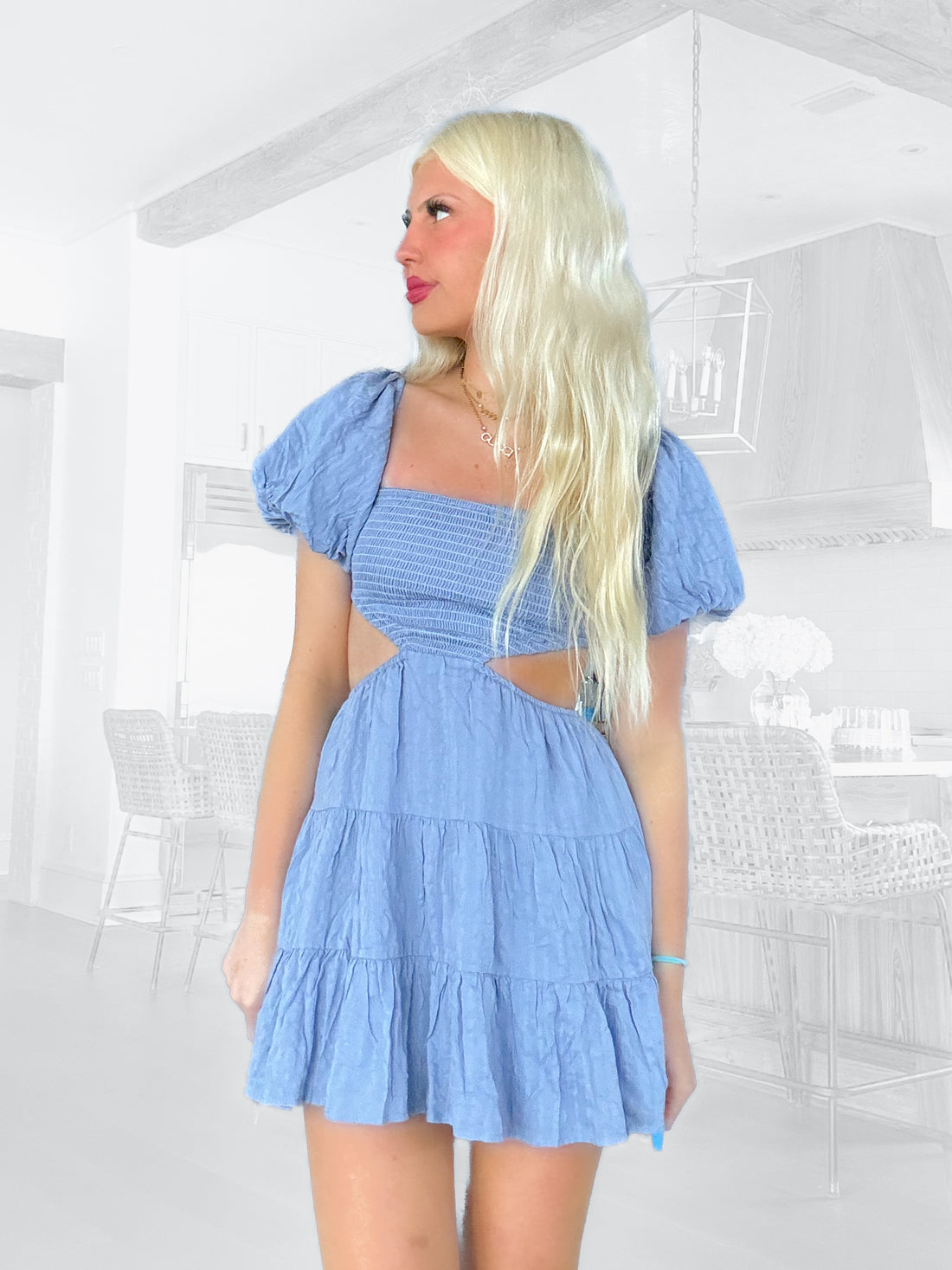 Cutout mini dress in slate blue, tiered ruffle skirt, puff sleeves, shown in a modern kitchen setting.
