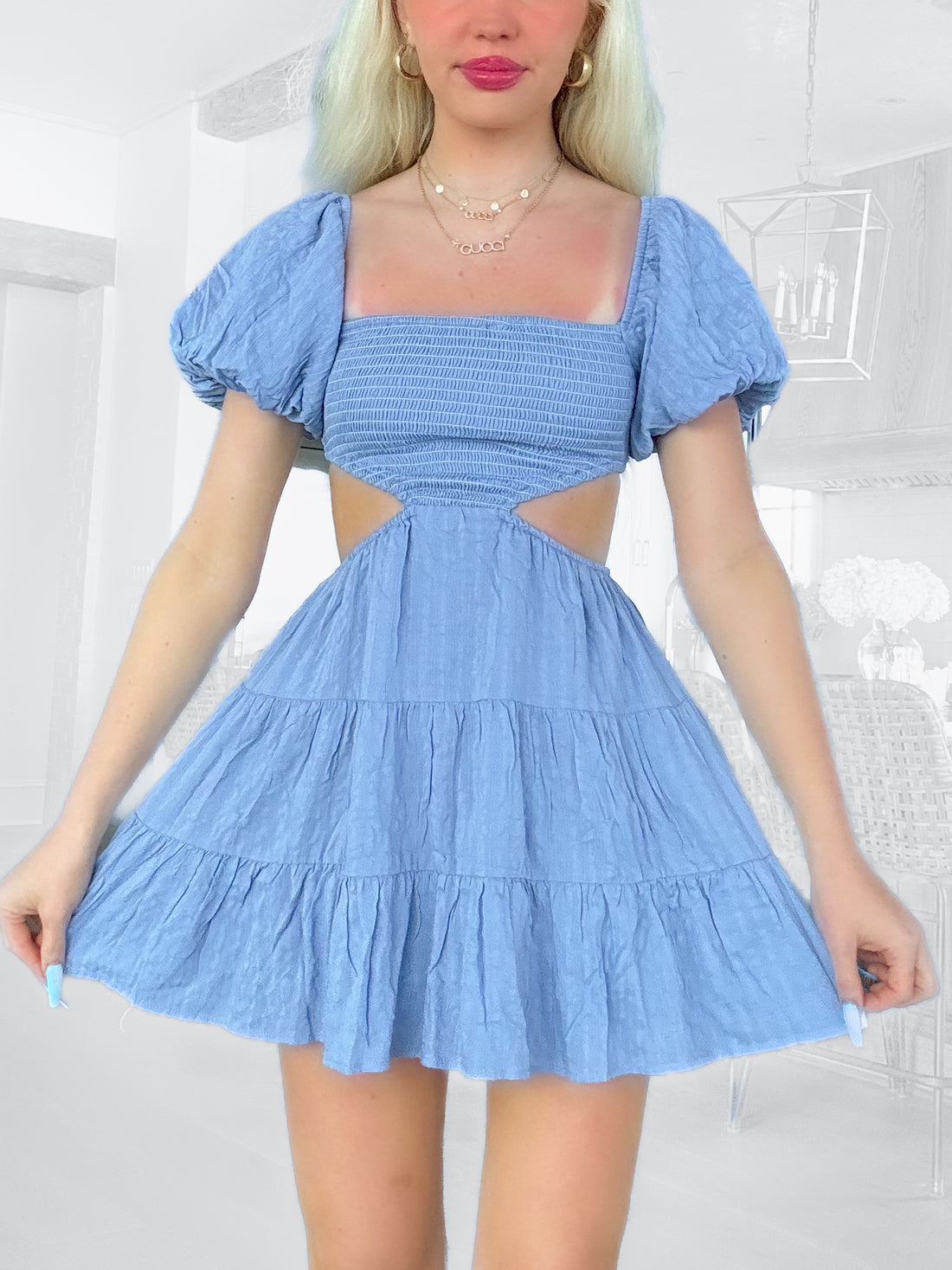 Light blue tiered mini dress with puff sleeves and cutout detail, shown on a model in a bright room.
