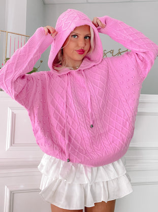 Pink cable-knit hooded sweater styled with a white ruffled skirt.
