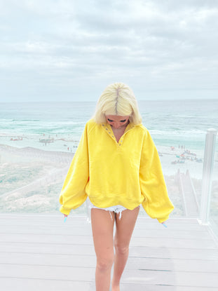 Yellow pullover sweater worn by a model on a beach boardwalk.
