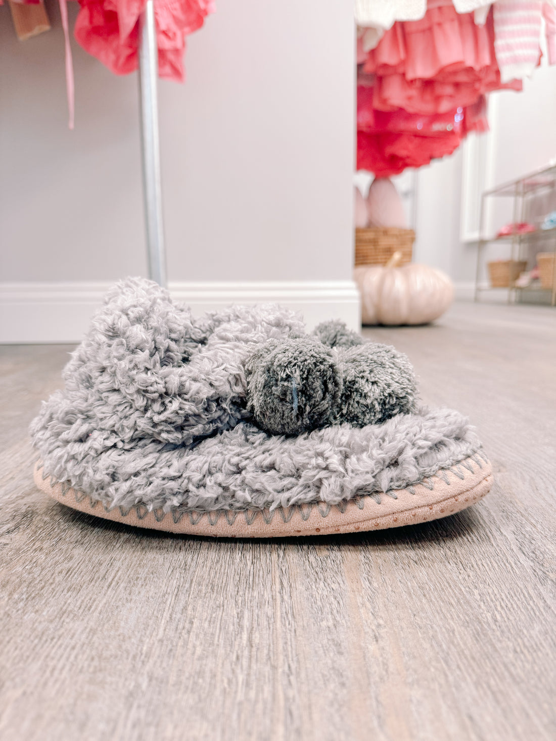 Cozy gray fuzzy slippers with pom-poms, resting on a wood floor.
