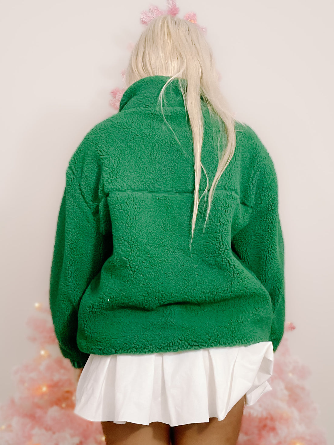 Deep green fleece jacket, half-zip style, shown from the back against a pink background.
