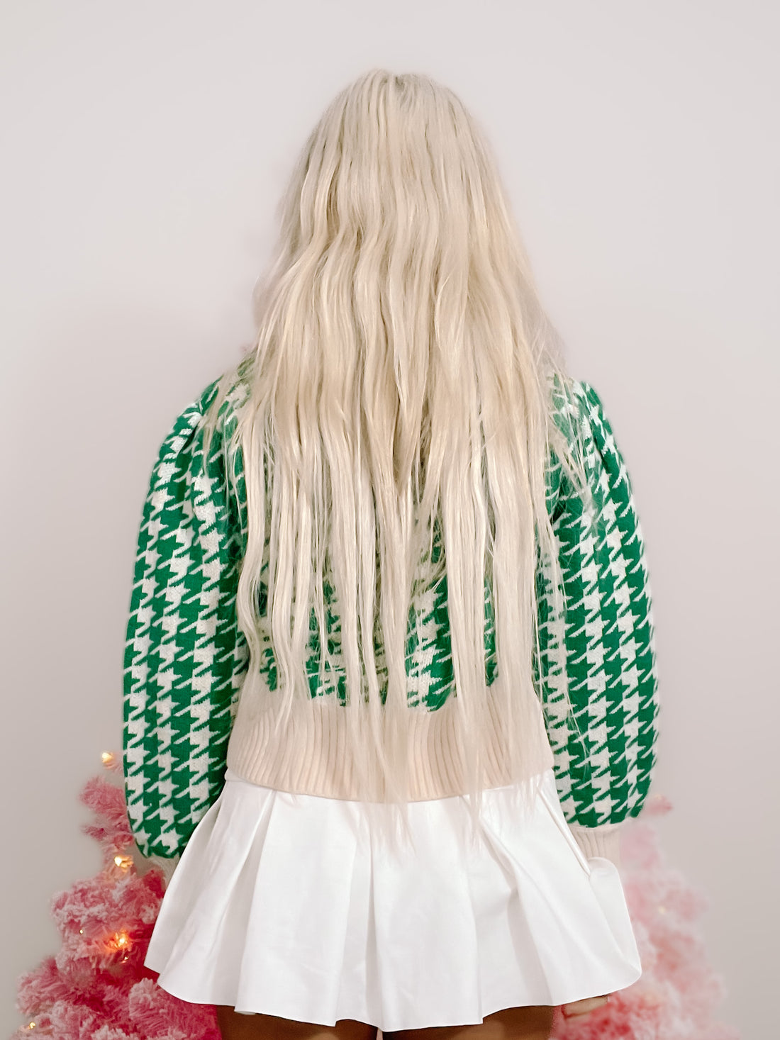 Green and white houndstooth knit cardigan, shown from the back, paired with a white pleated skirt.
