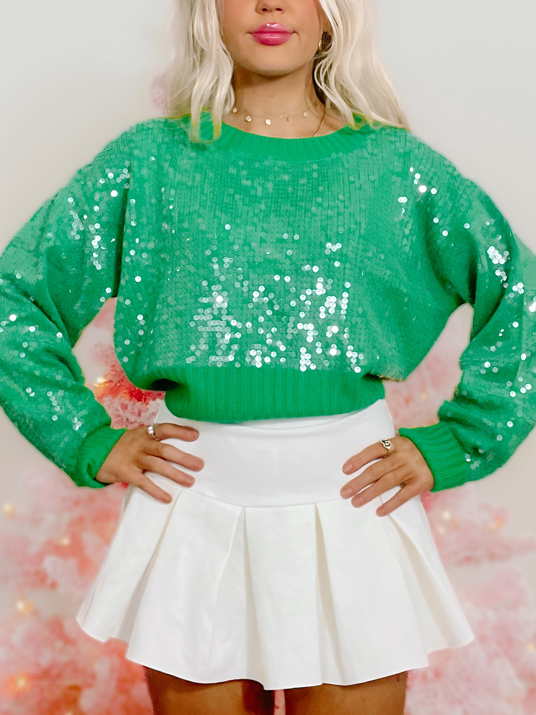 Green sequin sweater with long sleeves, modeled against a pink backdrop.
