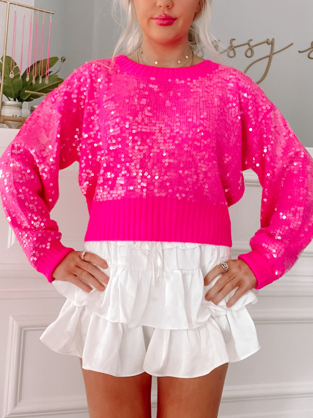Hot pink sequined sweater with long sleeves, shown paired with a white ruffled skirt.
