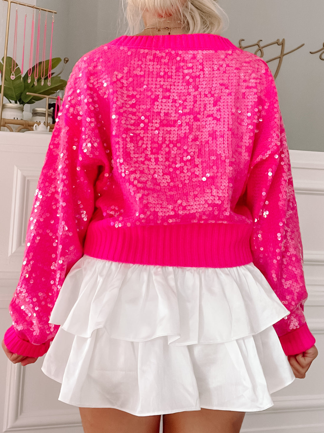 Hot pink sequin sweater with long sleeves, paired with a white ruffled mini skirt.
