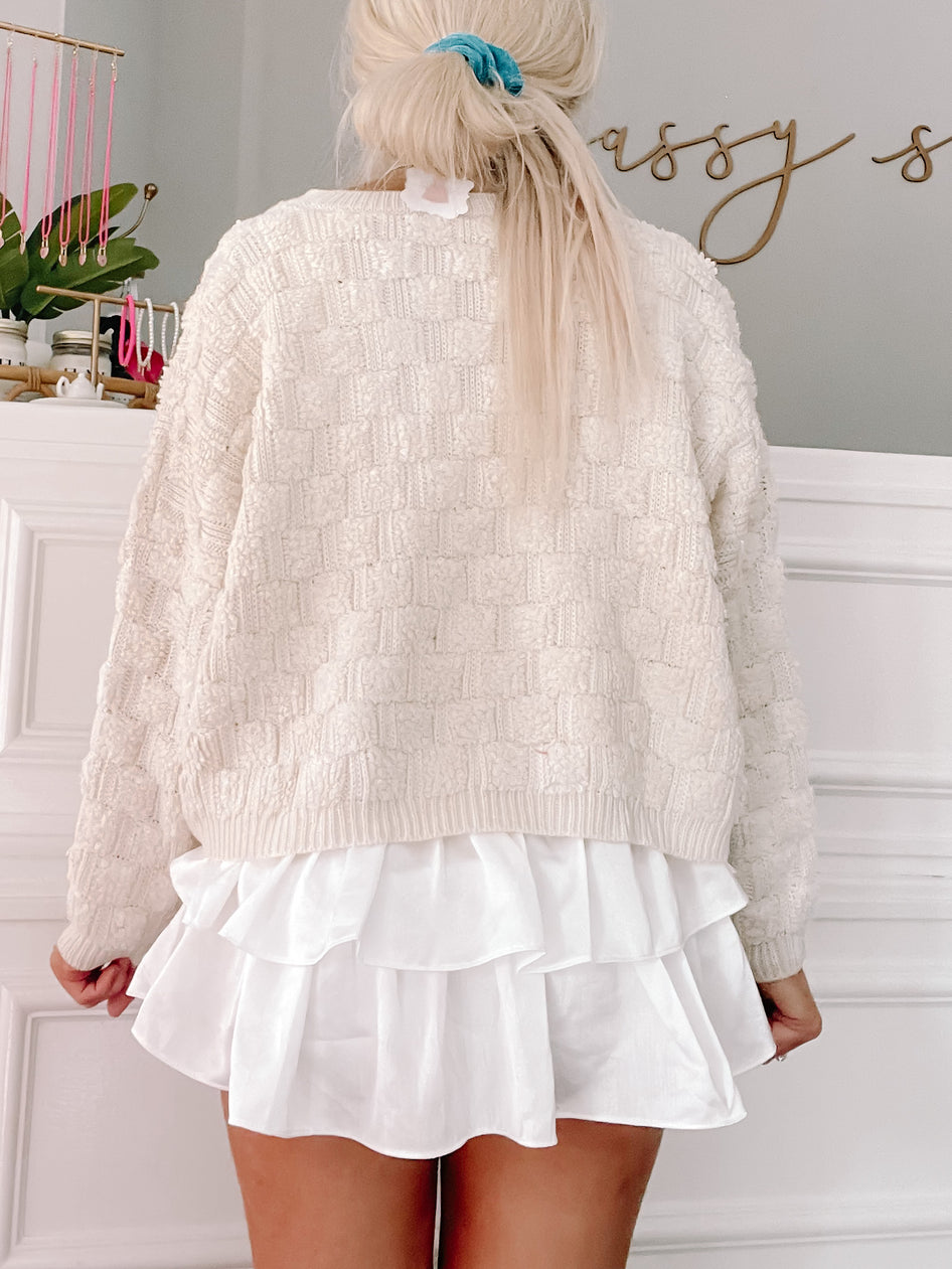 Cream textured knit sweater styled with a white ruffled mini skirt.

