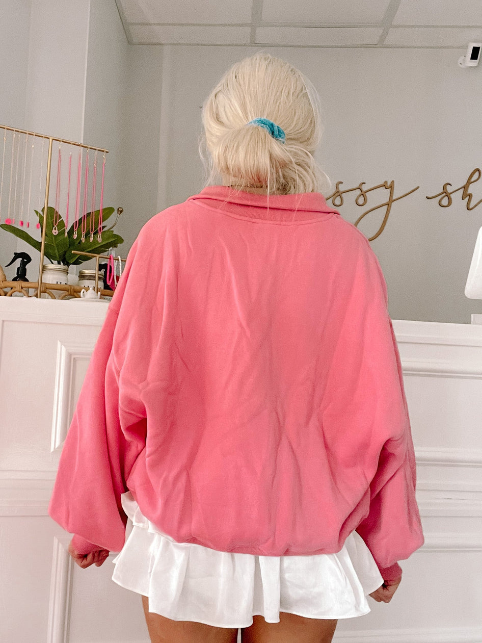 Pink half-zip sweatshirt shown from the back, styled with a white ruffle skirt.
