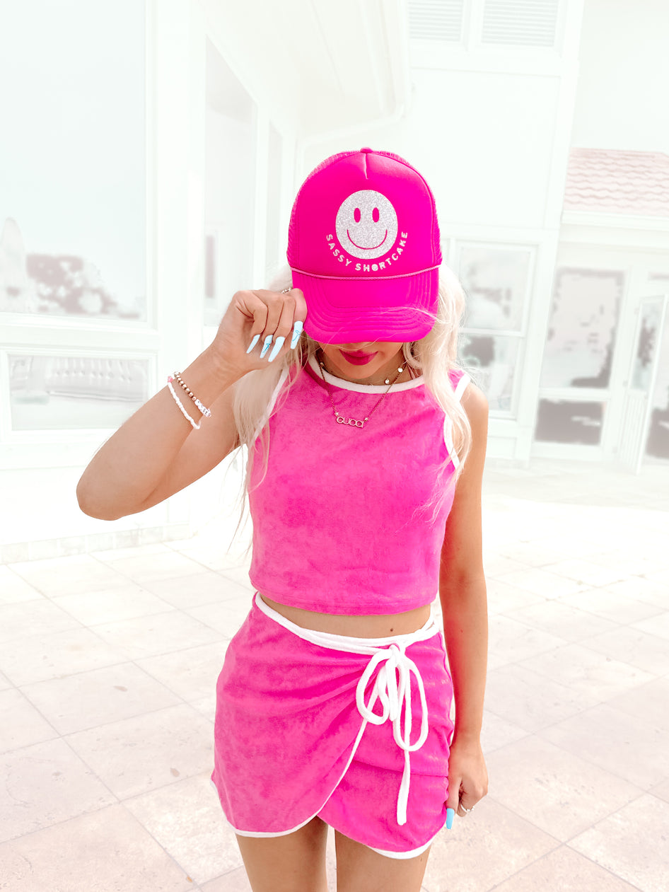 Hot pink velour crop top and mini skirt set; smiling face trucker hat
