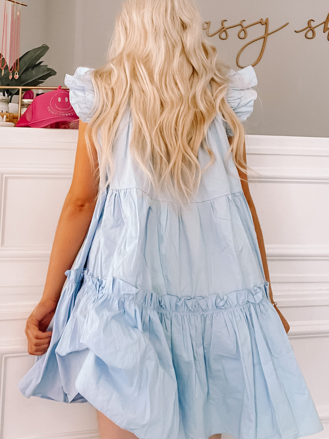 Light blue tiered mini dress with ruffle detailing, shown from the back against a white wall.
