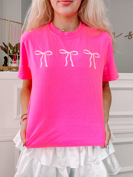 Hot pink Blushing Bow Tee featuring three white bows.
