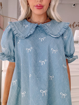 Light blue denim dress with embroidered bows and a ruffled Peter Pan collar.
