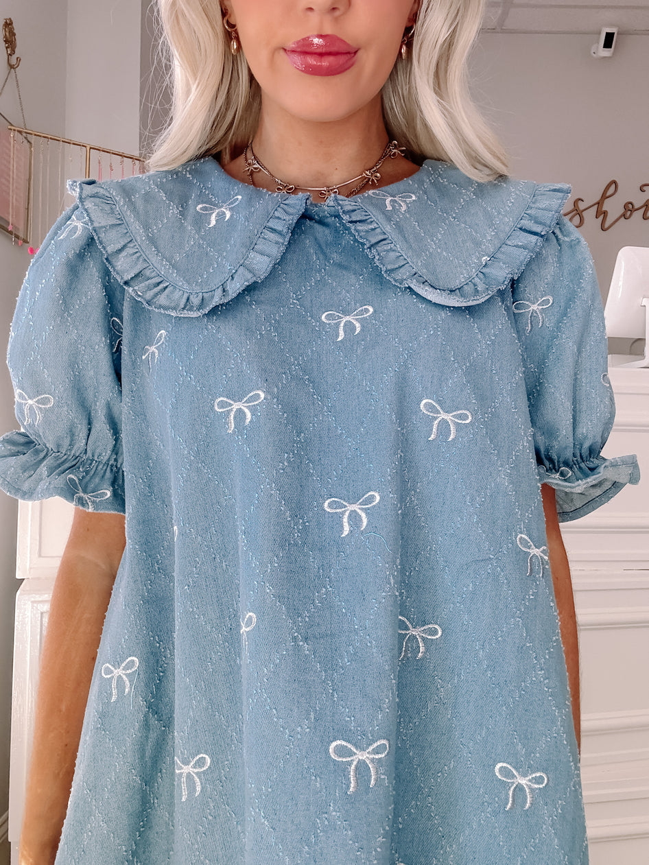 Light blue denim dress with embroidered bows and a ruffled Peter Pan collar.
