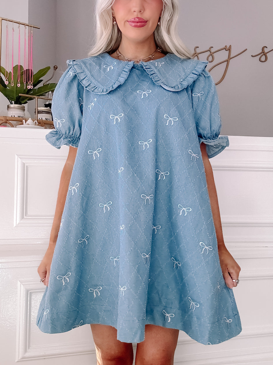 Light blue denim dress with white embroidered bows, Peter Pan collar, and short puff sleeves.

