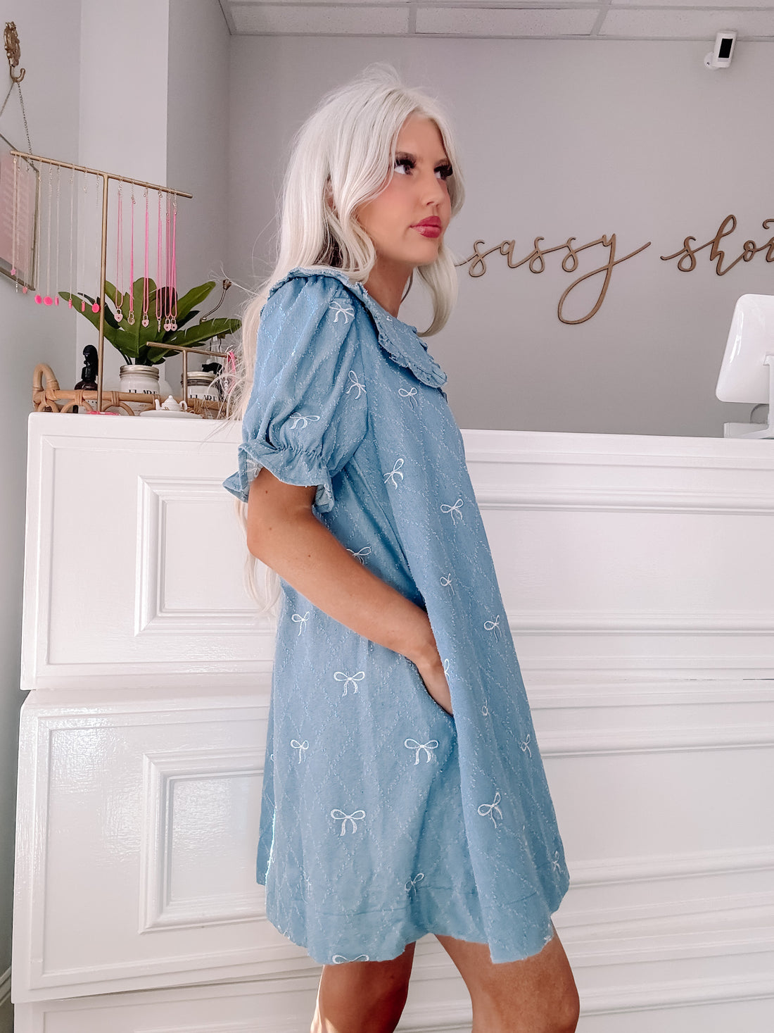 Light blue denim mini dress with embroidered white bows, modeled against a white backdrop - Denim Doll Dress from Sassy Shortcake
