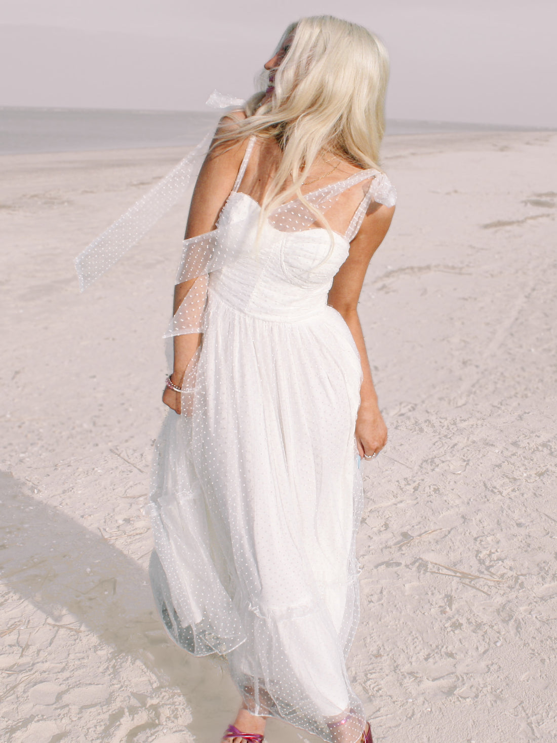 White polka-dot maxi dress on a sandy beach.
