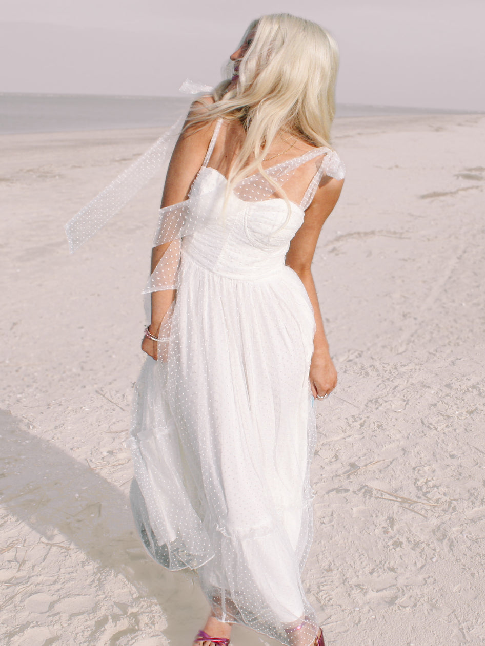 White polka-dot maxi dress on a sandy beach.
