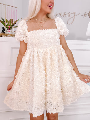 Cream-colored floral mini dress with short puff sleeves, shown on a model.
