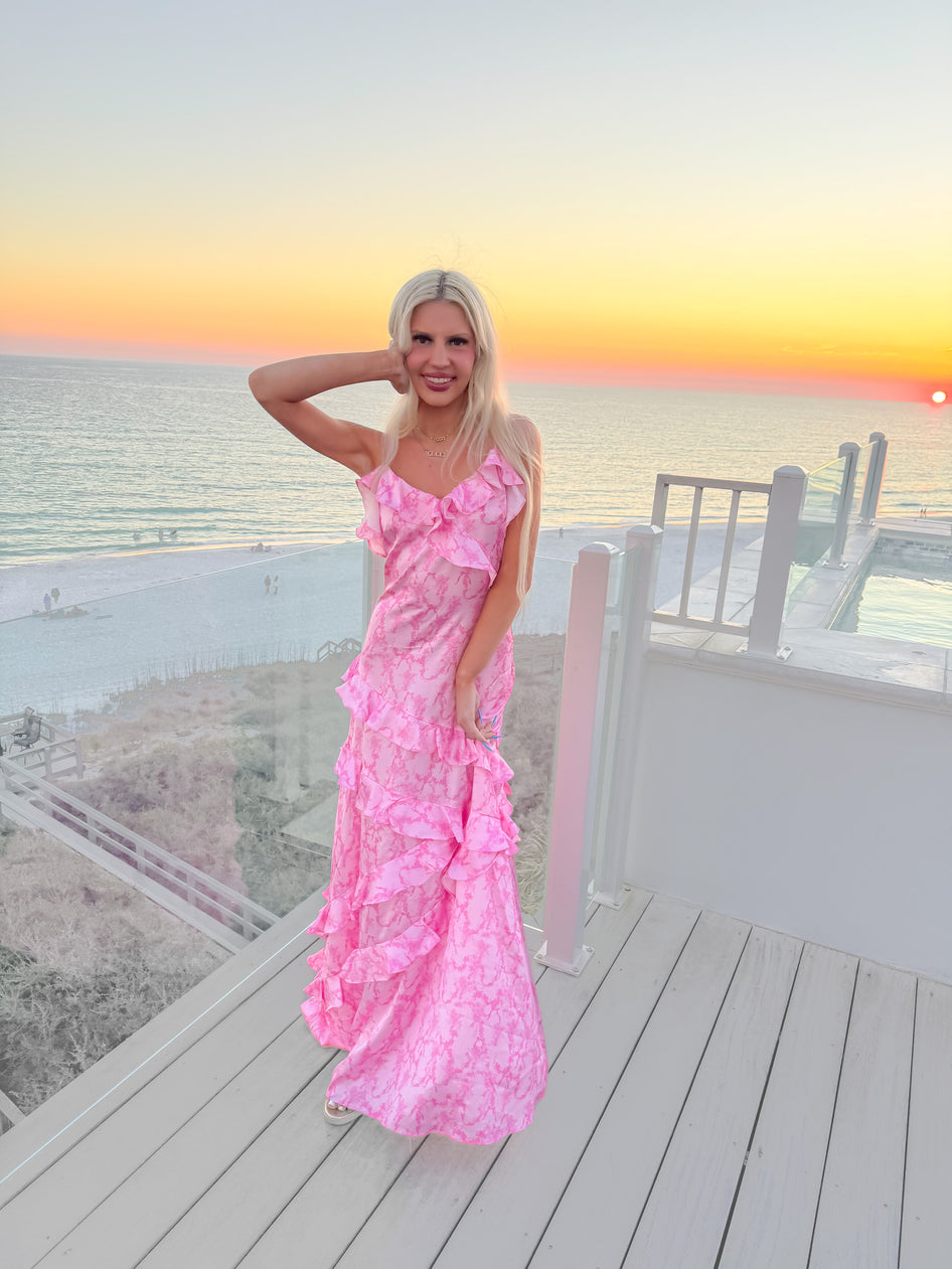 Pink tiered maxi dress on a beachside deck at sunset.
