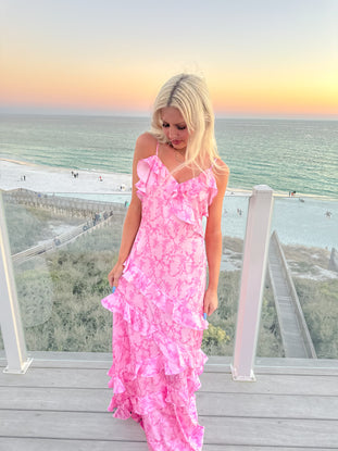 Pink tiered maxi dress on a balcony overlooking the ocean at sunset.

