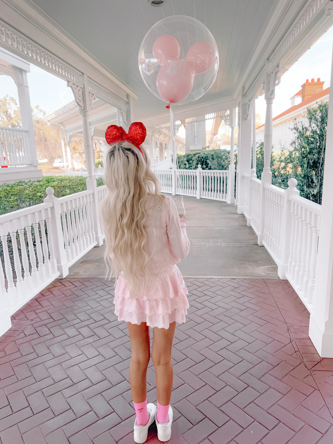 Girl in pink outfit on a brick walkway, holding a Mickey Mouse balloon.
