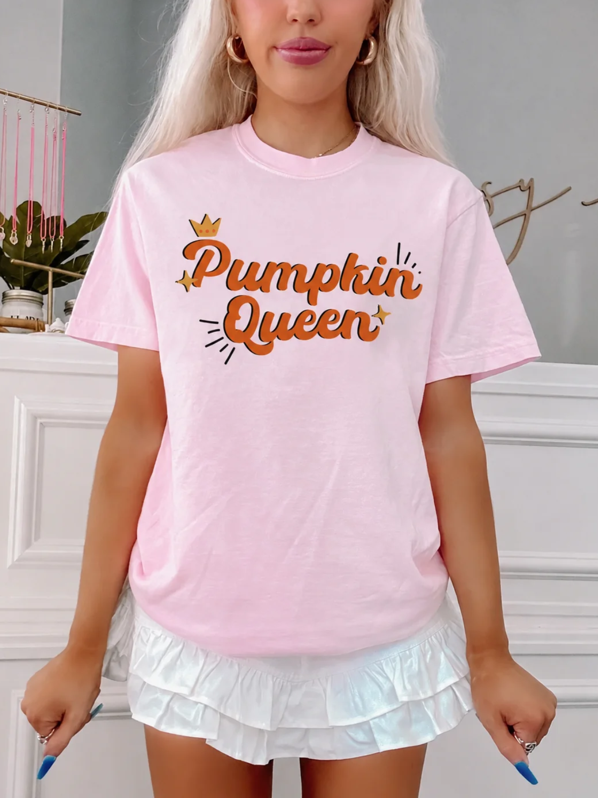 Model wearing the Pumpkin Queen Tee from Sassy Shortcake, a light pink fall graphic tee with orange retro Pumpkin Queen script and a gold crown, styled with a white ruffle skirt.