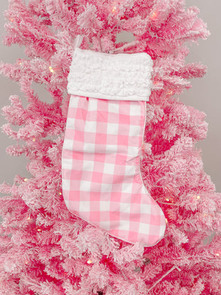 Pink gingham Christmas stocking with white ruffle, hanging on a pink flocked artificial tree.
