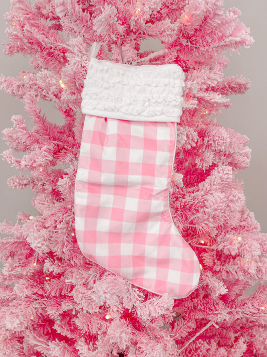 Pink gingham Christmas stocking with white ruffle, hanging on a pink flocked artificial tree.
