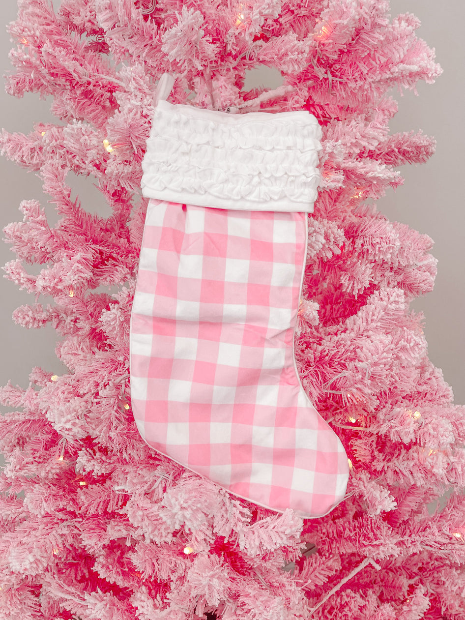 Pink gingham Christmas stocking with white ruffle, hanging on a pink flocked artificial tree.
