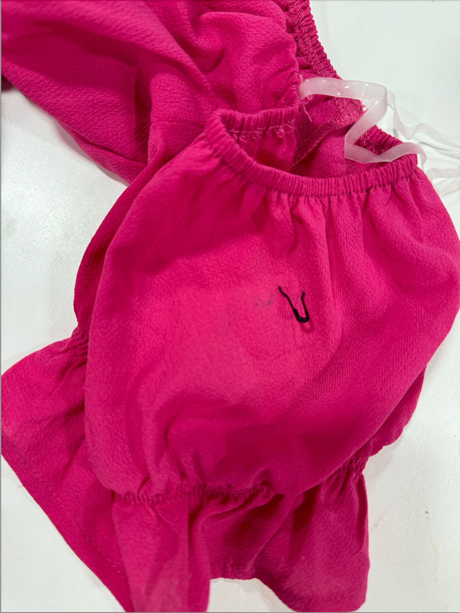 Close-up of hot pink fabric with ruffled detailing and a small imperfection.
