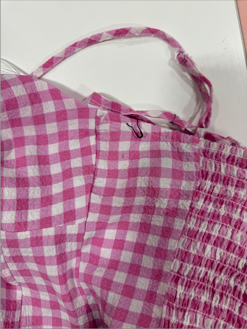 Close-up of pink and white gingham fabric detail, showing shoulder straps and gathers.
