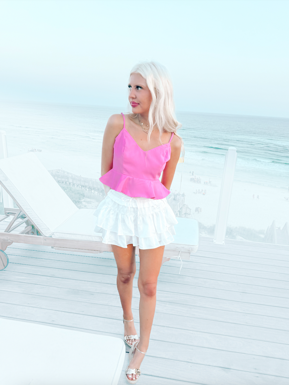 Pink satin camisole top paired with a white ruffled mini skirt, ocean view backdrop.
