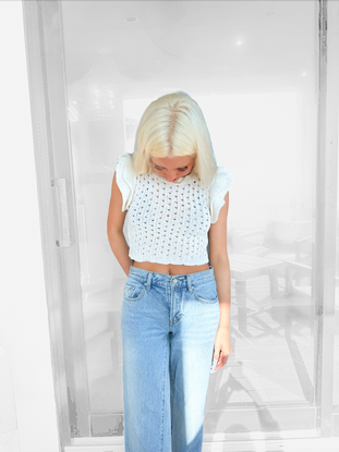 White open-knit cropped top with ruffle sleeves, modeled against a blurred background.
